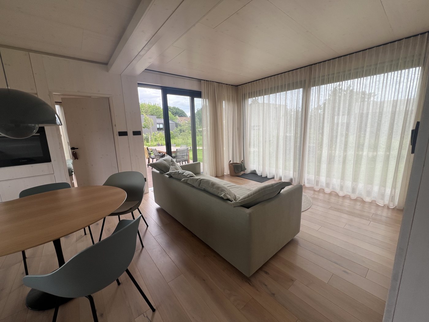 Living area with sofa in front of sheer curtains, the round dining table in the foreground