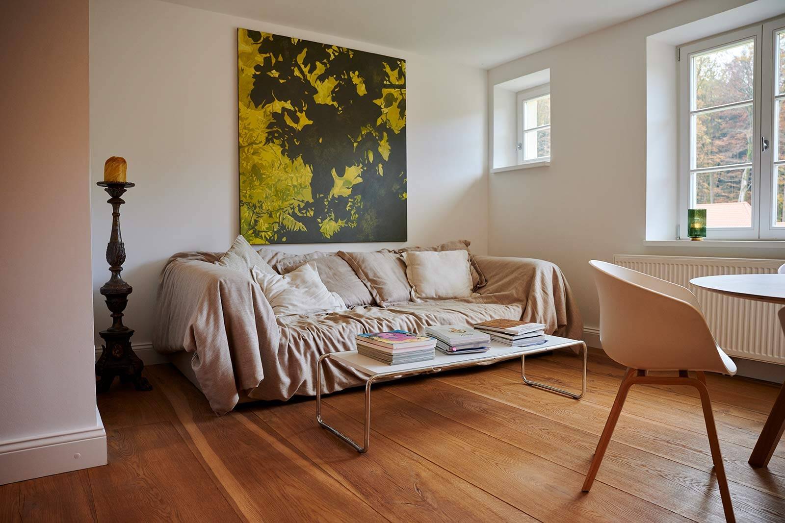 Living area with sofa, large-format yellow artwork and wooden floorboards